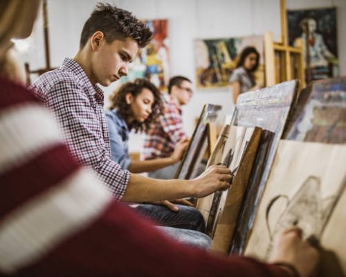 Group of students drawing their paintings on a class at art studio. Focus is on male student.